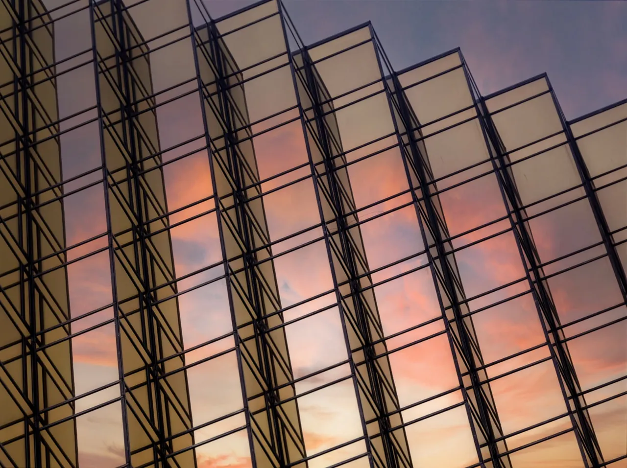 Glass panels on an office building reflecting a warm sunset.